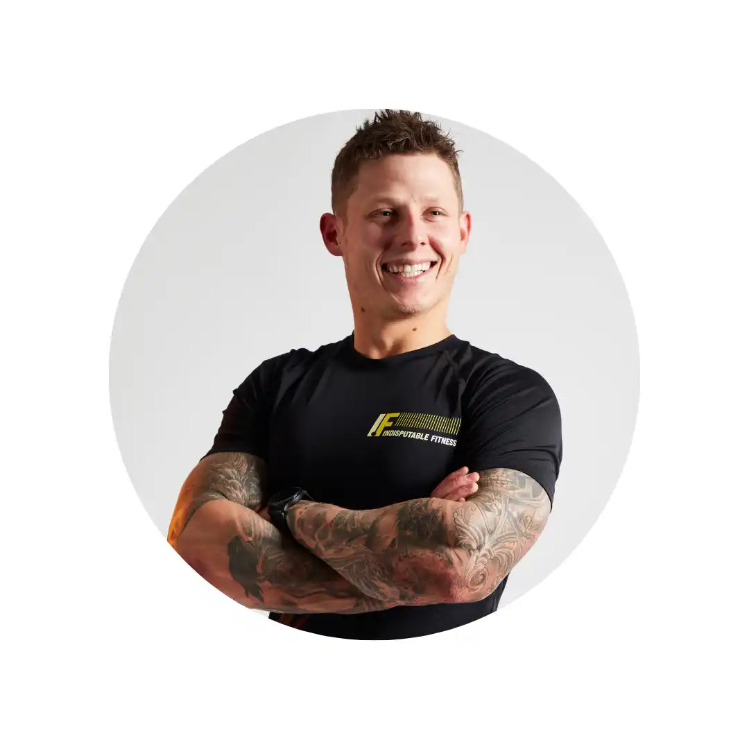 A smiling person in a black t-shirt with tattooed arms crossed over their chest.